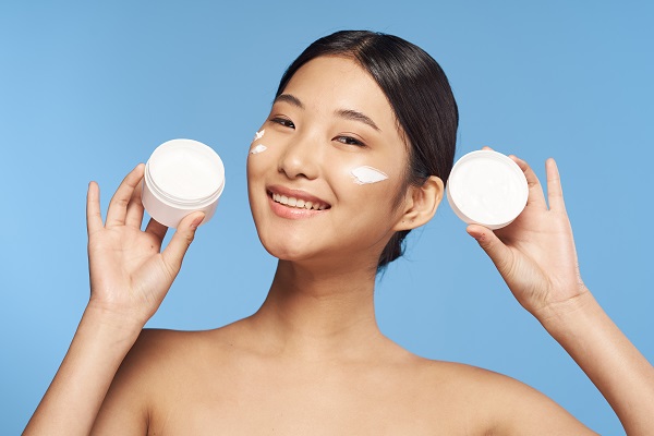 Woman holding moisturizer with cream on her face