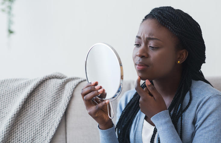 A picture of a black woman examining her chin in the mirror.