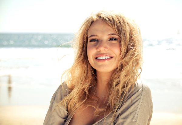 A young blonde woman at the beach smiles at the camera